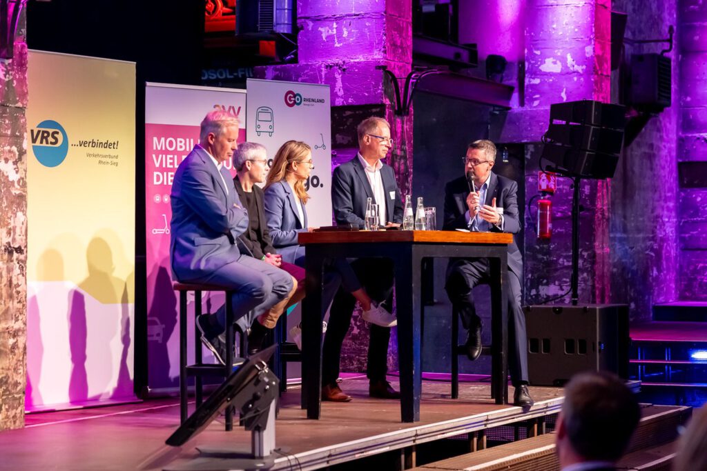 Moderatorin für Nachhaltigkeit, ESG & Transformation Janine Utsch an einem hohen Tisch sitzend bei der Moderation eines Panels bei Go.Rheinland - Mobilitätsakademie