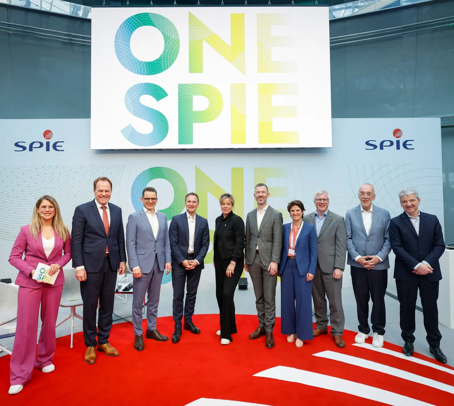 Moderatorin für Nachhaltigkeit, ESG & Transformation Janine Utsch im pinkfarbenen Anzug bei der Moderation der Messe "OneSpie", neben ihr teilnehmende Experten