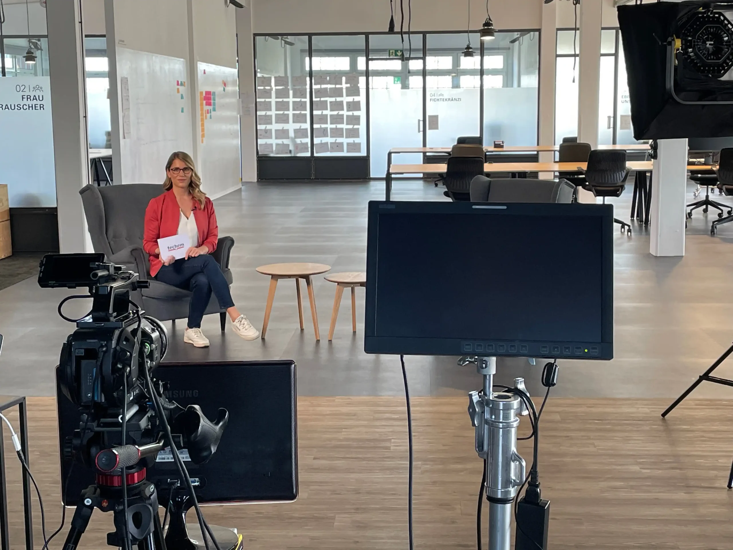 Web TV Moderatorin Janine Utsch auf einem Sessel sitzend, im Vordergrund mehrere Kameras und Bildschirme für die Aufzeichnung