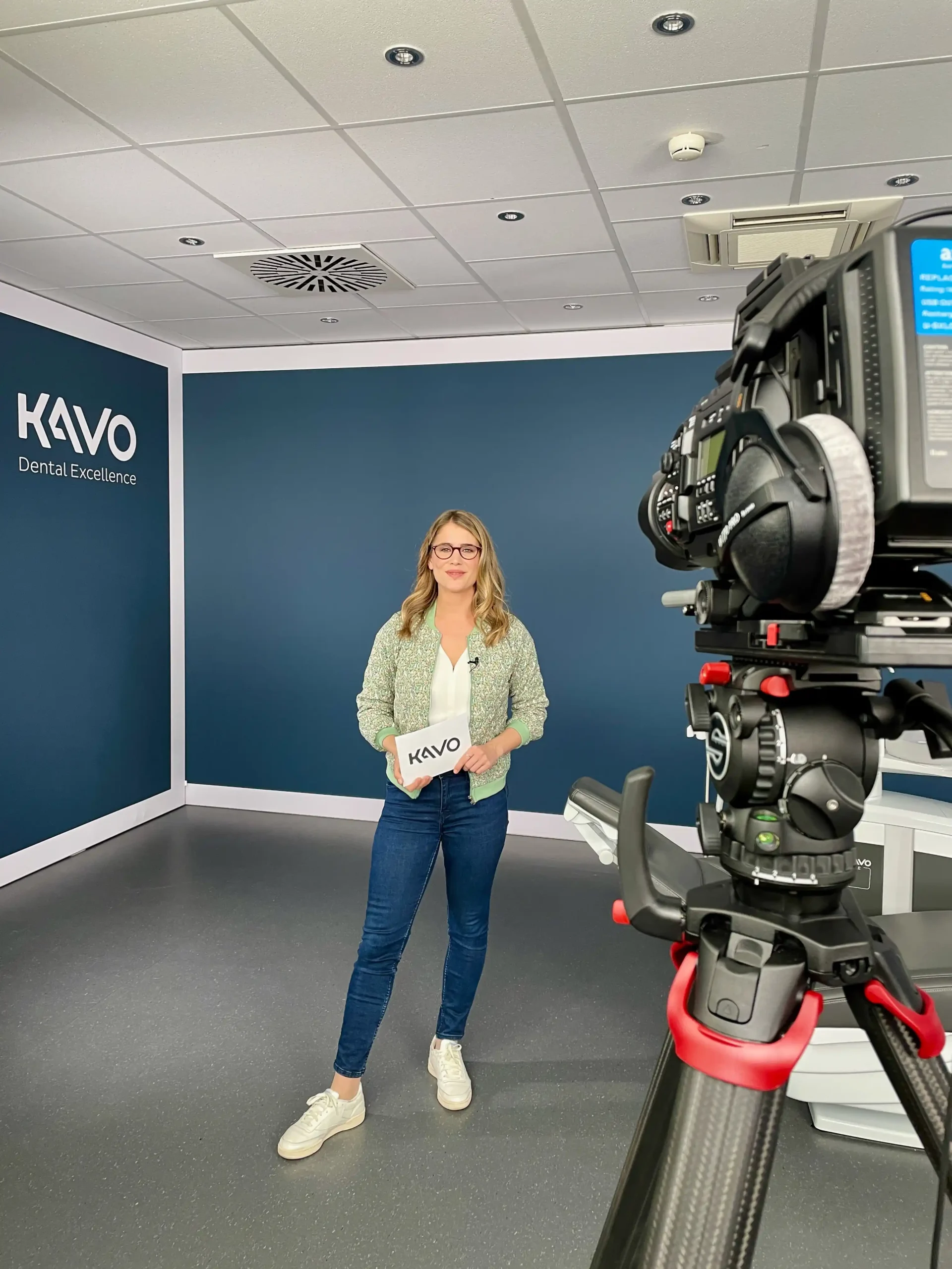 TV Moderatorin Janine Utsch vor einer dunkelblauen Wand, im Vordergrund eine Fernsehkamera